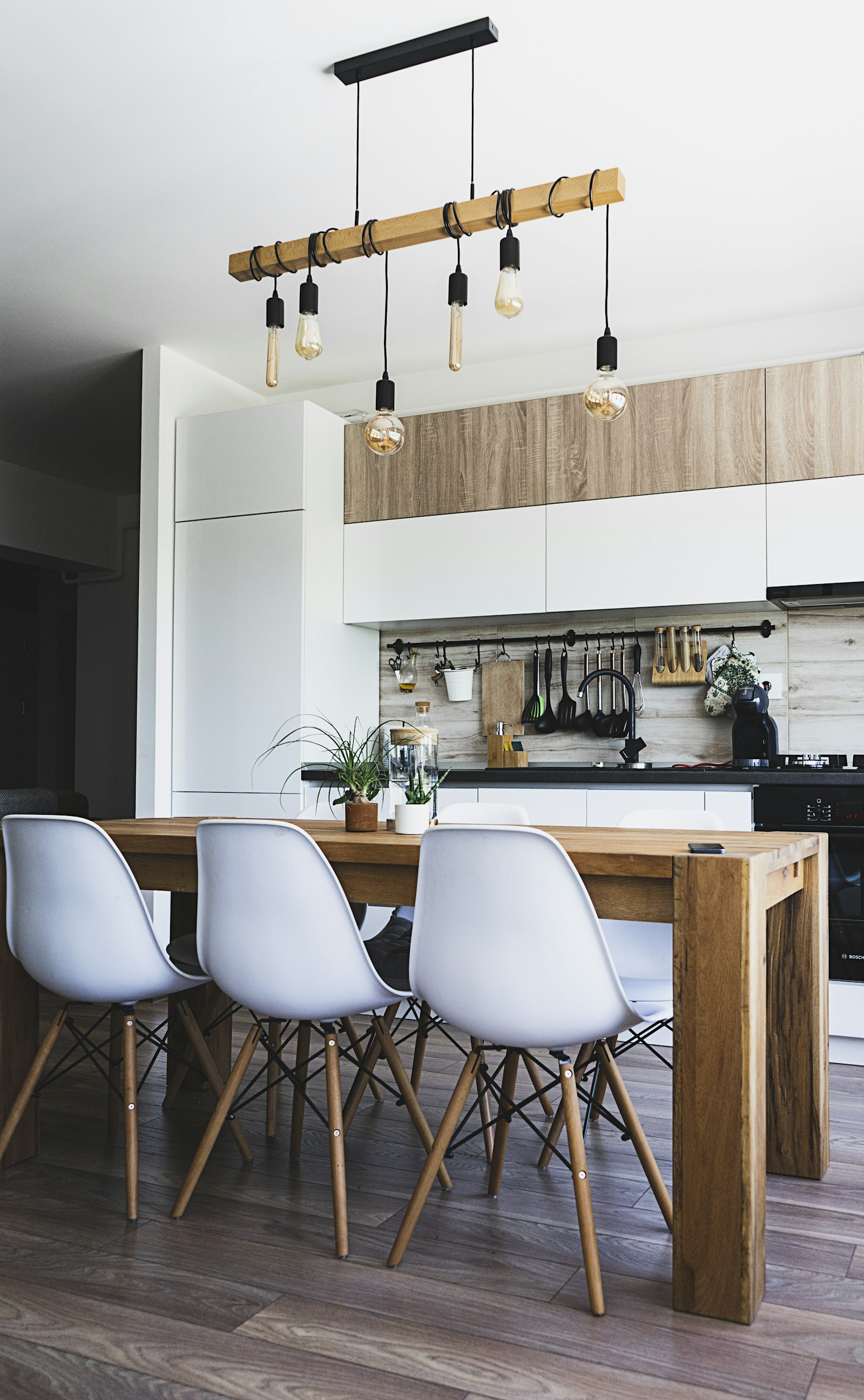 Brown wooden dining table with white chairs near a kitchen